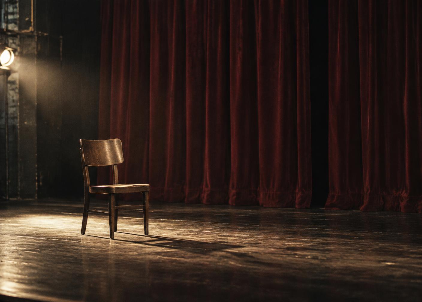 A solitary chair on a theatre stage before deep red curtains